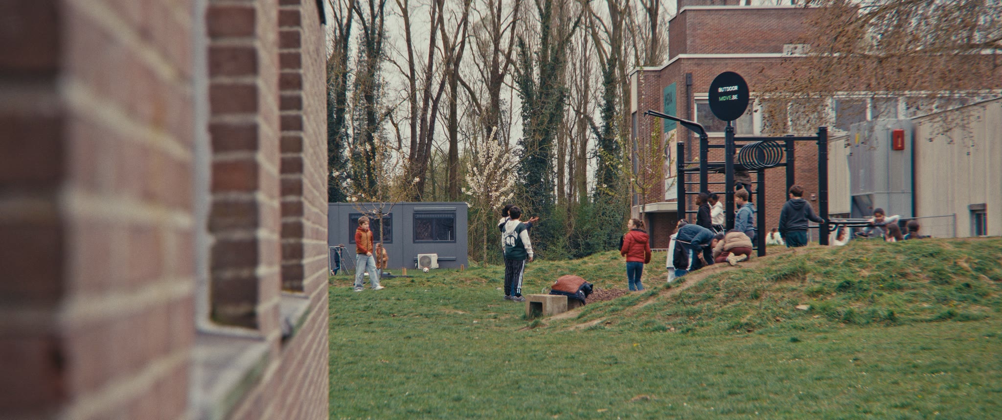 Leerlingen op de speelplaats, tussen de bomen achter de school.