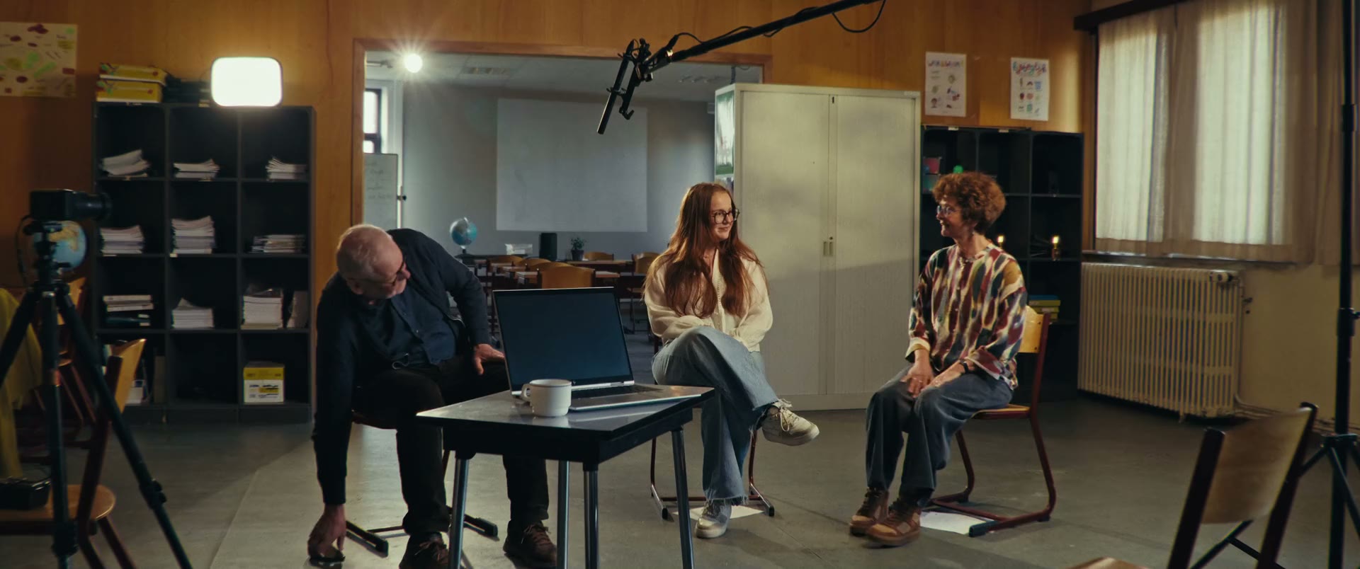 De filmploeg in gesprek met twee leerlingen, op stoelen in een klaslokaal.